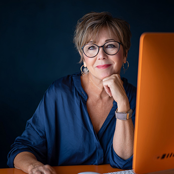 Frau lächelt in die Kamera. Vor ihr steht ein Computer.